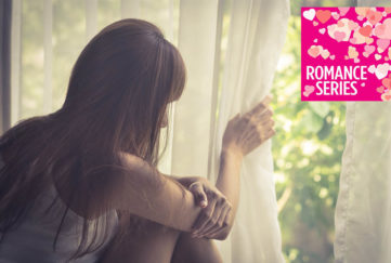 Long haired girl lifting net curtain to look out of window