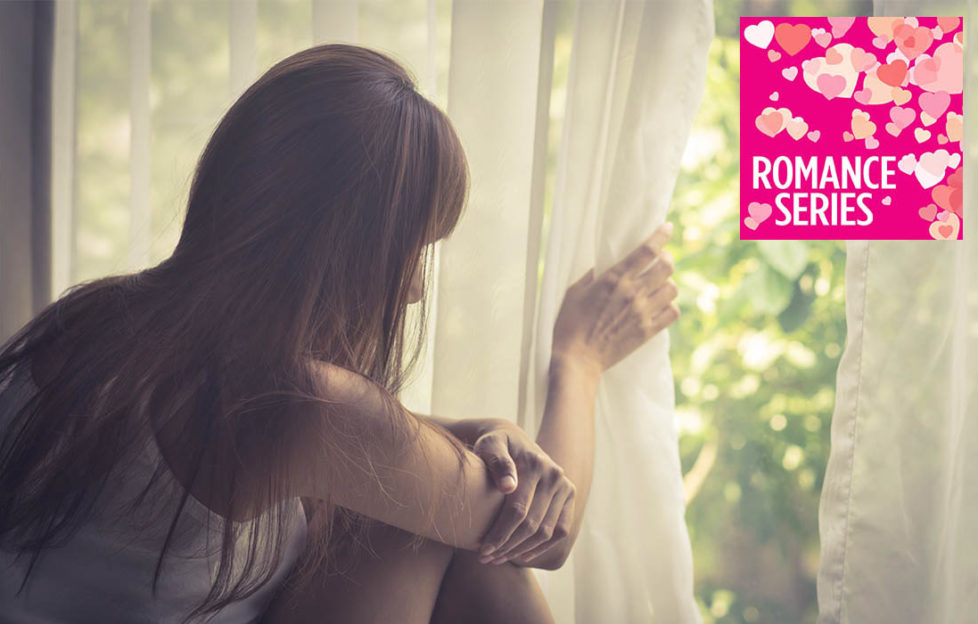 Long haired girl lifting net curtain to look out of window