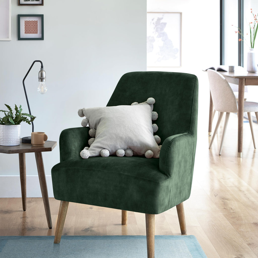 Deeply padded dark green armchair on wooden legs with cream cushion edged with large pom poms