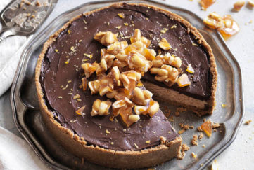Chocolate cheesecake, topped with a pile of caramelised nuts, one slice cut