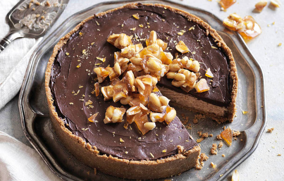Chocolate gluten-free cheesecake, topped with a pile of caramelised nuts, one slice cut