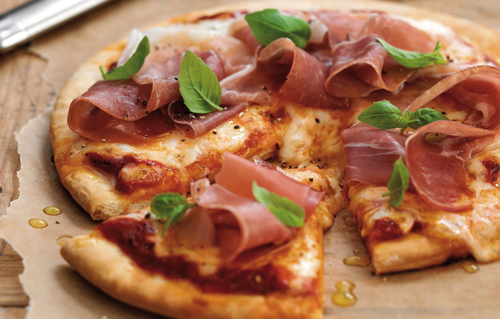 Pizza decorated with ham and basil leaves, one slice cut