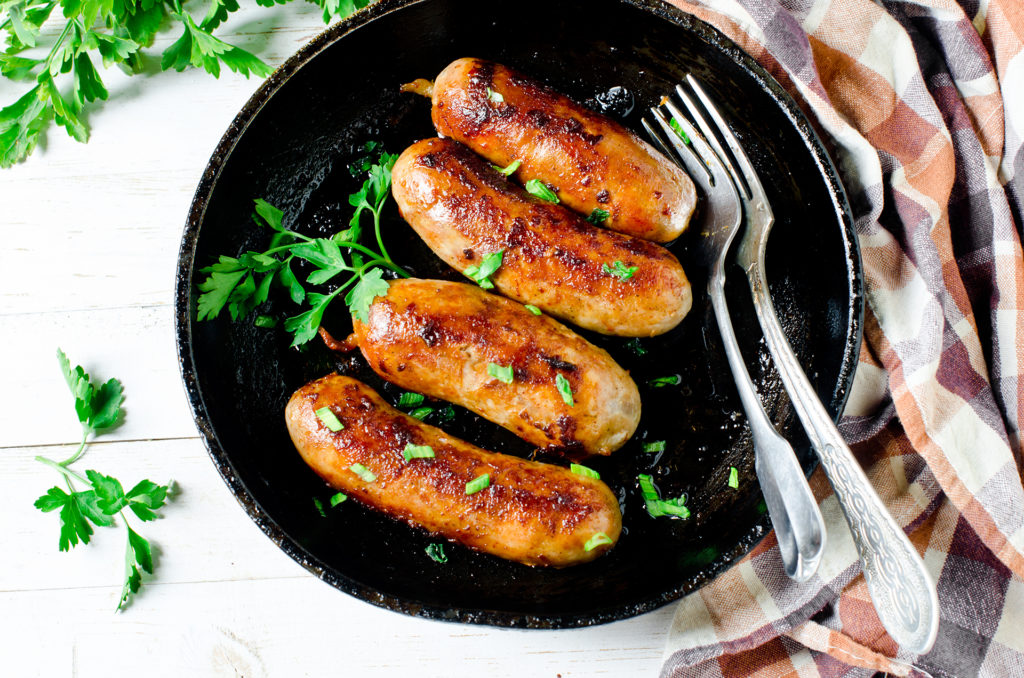 4 sausages cooking in frying pan