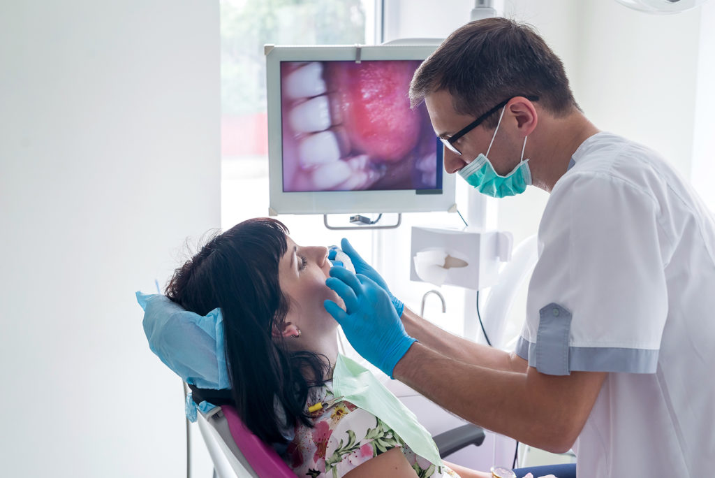 Dentist checking patient's teeth with intraoral camera; 