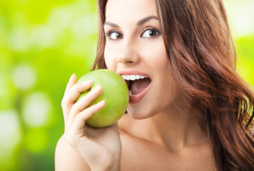 Woman biting into green apple outdoors