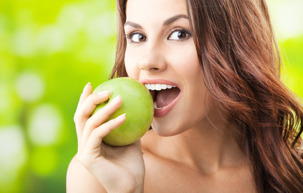 Woman biting into green apple outdoors