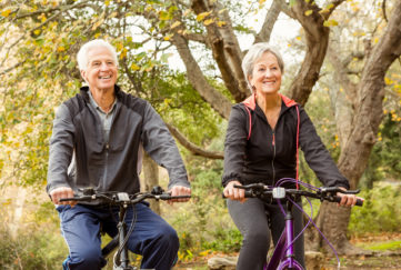 Senior couple cycling in the park as cycling is a good way to keep your waist during menopause