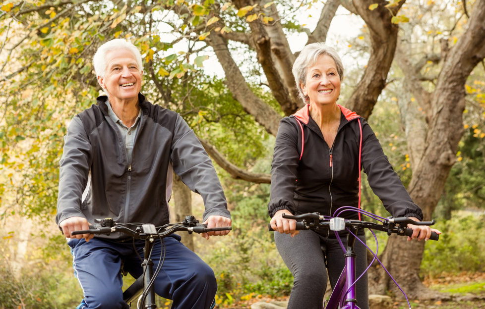 Senior couple cycling in the park as cycling is a good way to keep your waist during menopause
