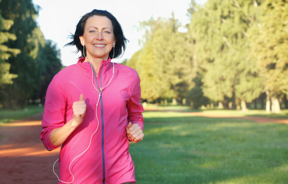 Portrait of elderly woman running with headphones in the park in early morning. Attractive looking mature woman keeping fit and healthy