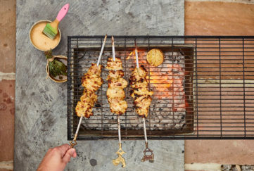 Three skewers of chicken chunks in creamy sauce being grilled over a barbecue