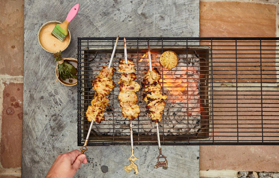 Three skewers of chicken chunks in creamy sauce being grilled over a barbecue