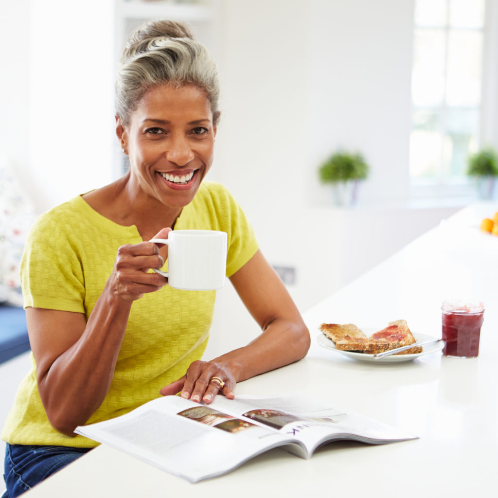 Smiling mature woman with coffee and toast, reading magazine, me-time