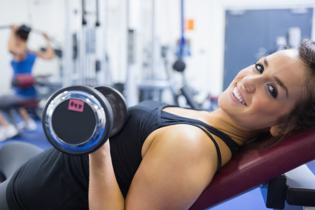 Woman lying on bench at gym lifting weight