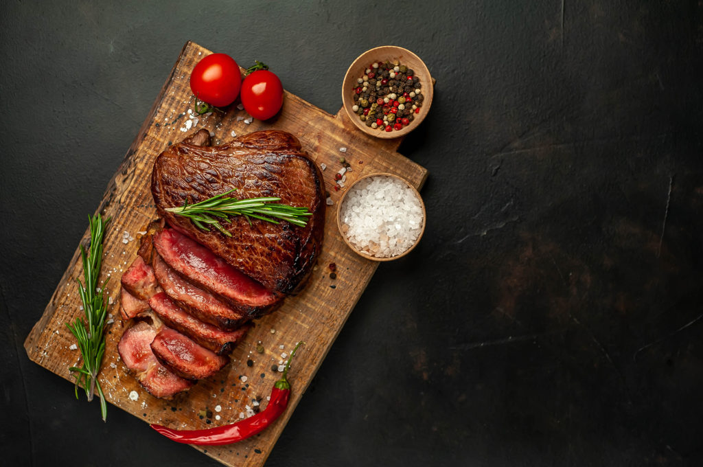 Beef steak, herbs and spices on a cutting board on a background of stone,