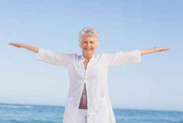 Casual senior woman with arms outstretched standing at the beach