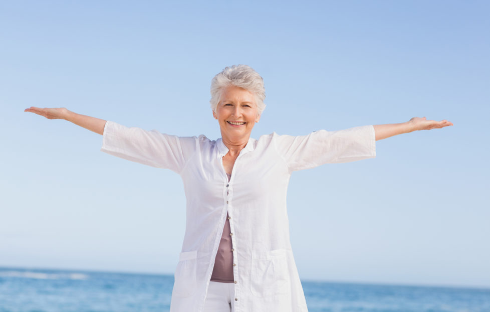Casual senior woman with arms outstretched standing at the beach
