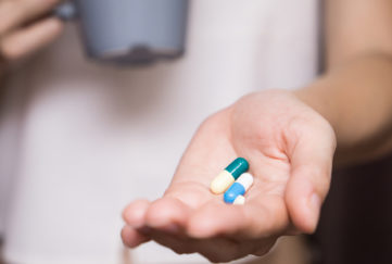 Woman's hand with pills in it and mug in other hand