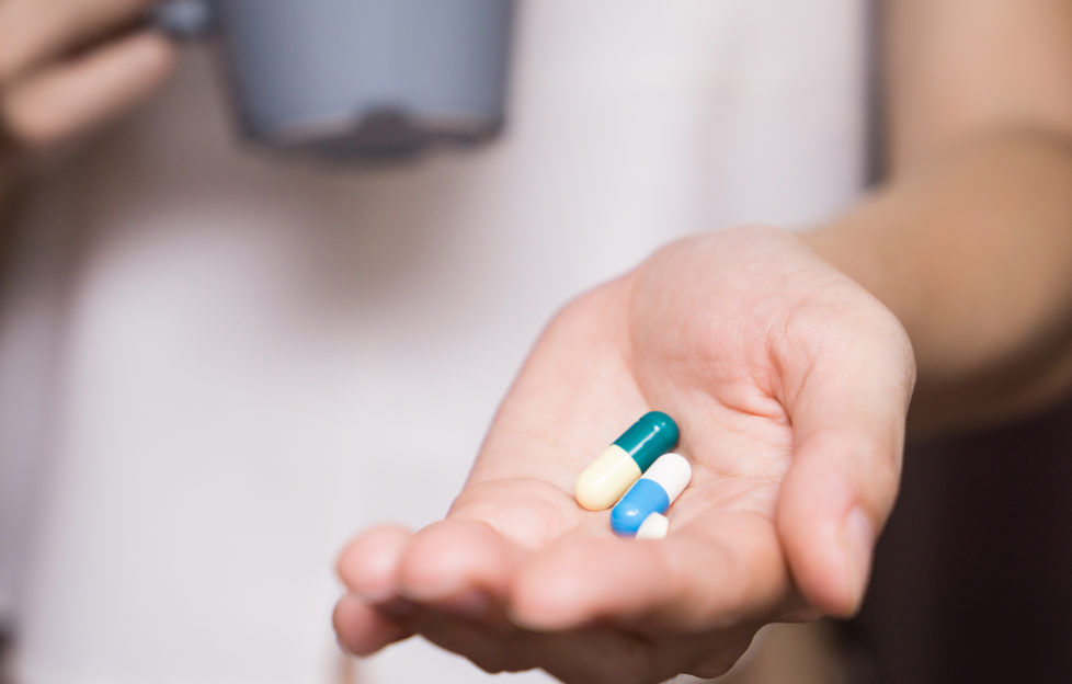 Woman's hand with pills in it and mug in other hand