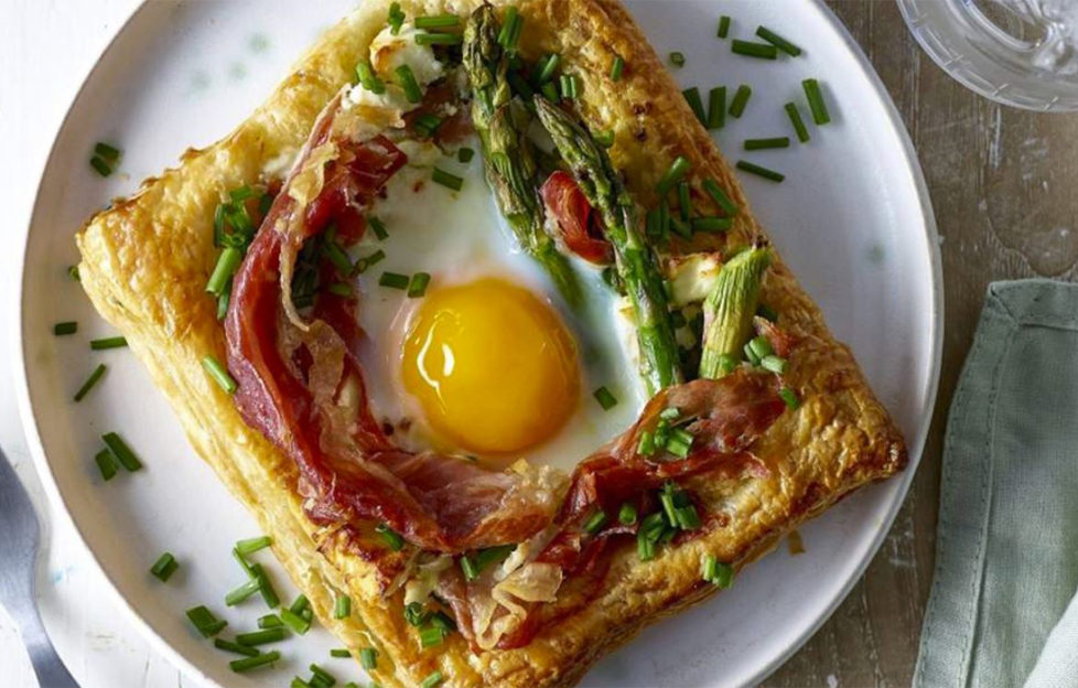 Square of golden puff pastry topped with baked egg, asparagus, melted feta cheese and herbs