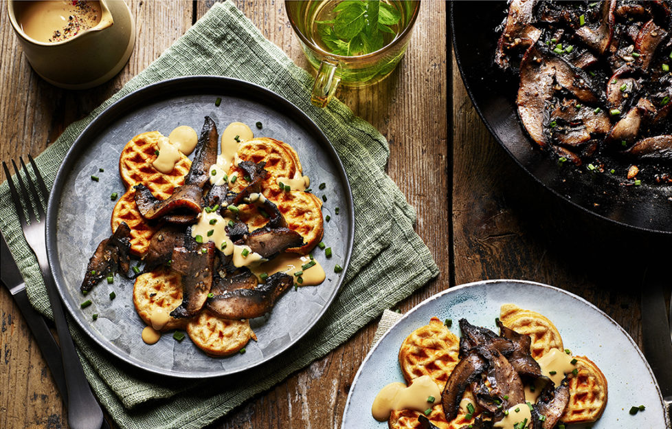 2 plates of small round golden waffles with rich brown mushrooms and creamy dressing