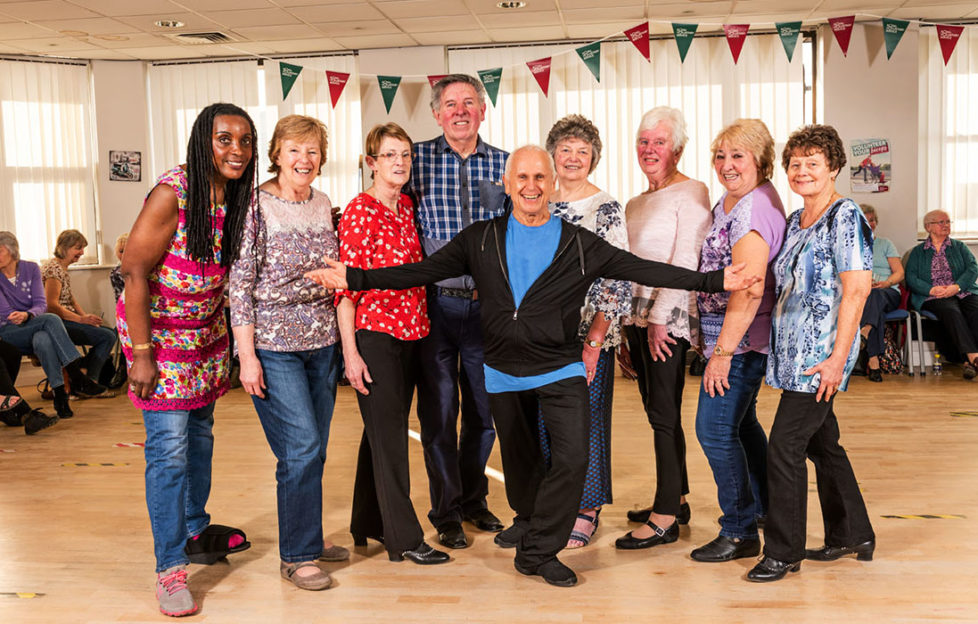 Ballet dancer Wayne Sleep in casual dancewear with 7 smiling mature ladies and one man at class run by Royal Voluntary Service