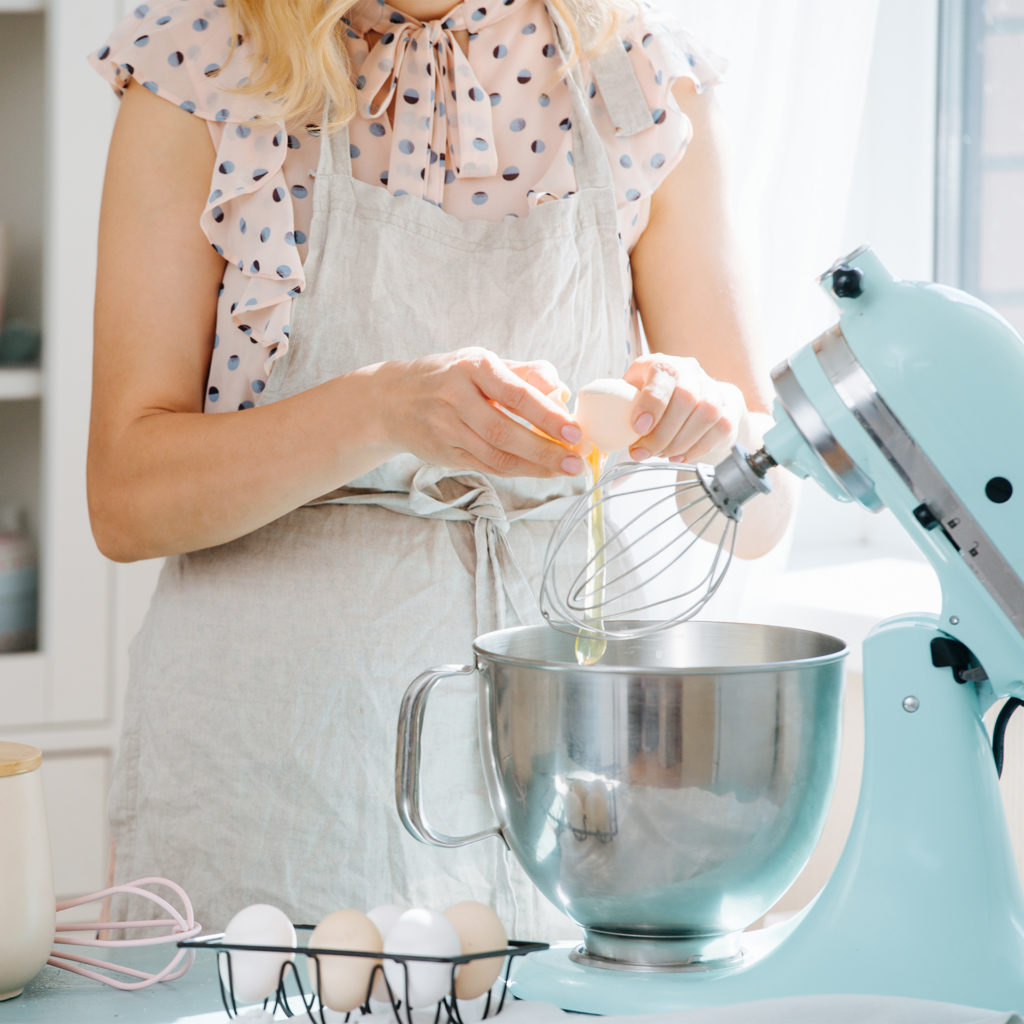 Woman cracking eggs into bowl of a retro style sky blue kitchen mixer