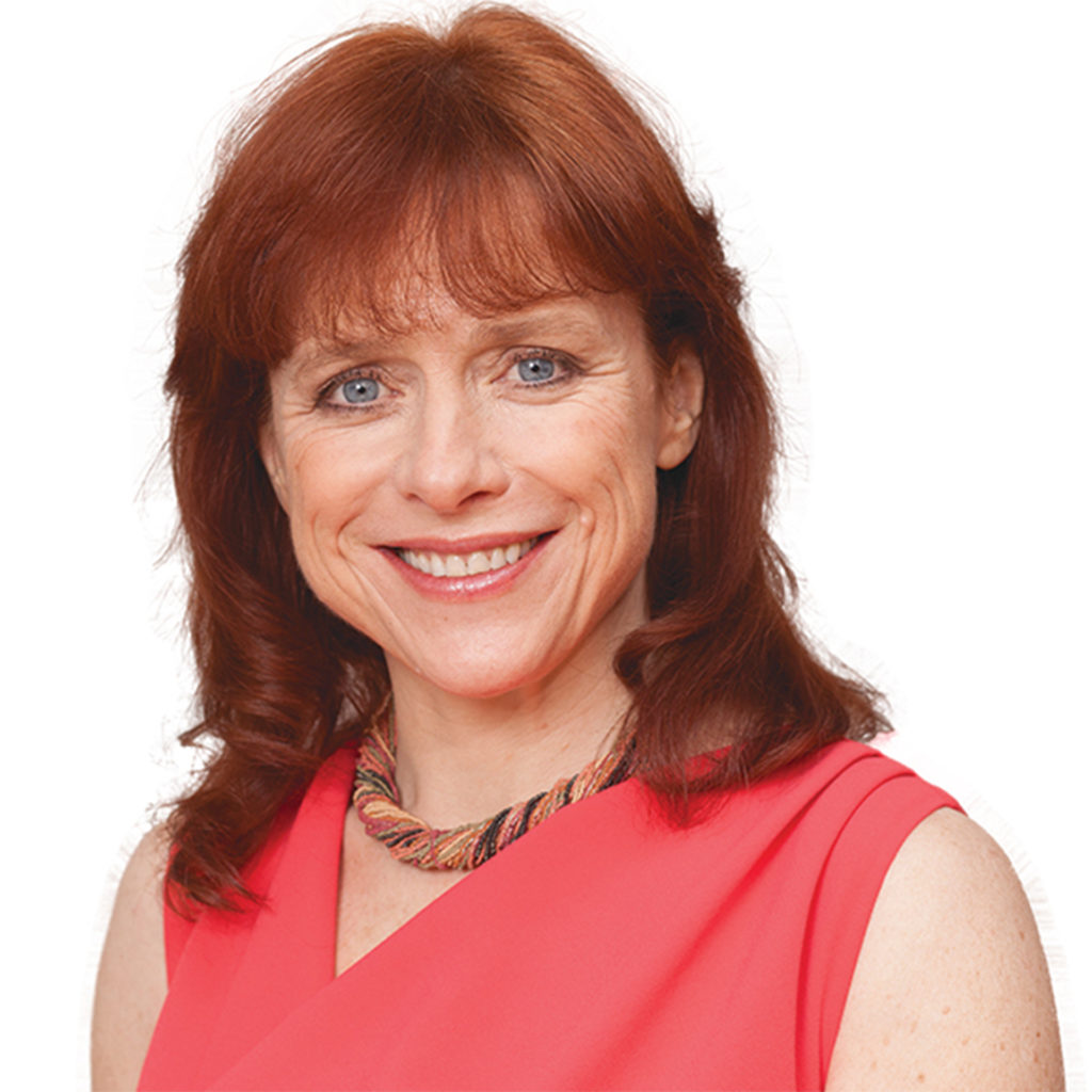 Portrait shot of Dr Sarah Jarvis, smiling relaxed woman in 40s with shoulder length auburn hair, blue eyes and red sleeveless blouse