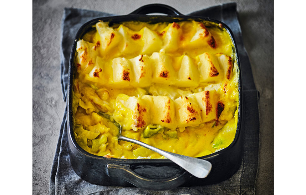 Black oven dish with handles, full of golden fish pie, mash on top arranged in stepped rows, fish and leeks in creamy golden sauce underneath.
