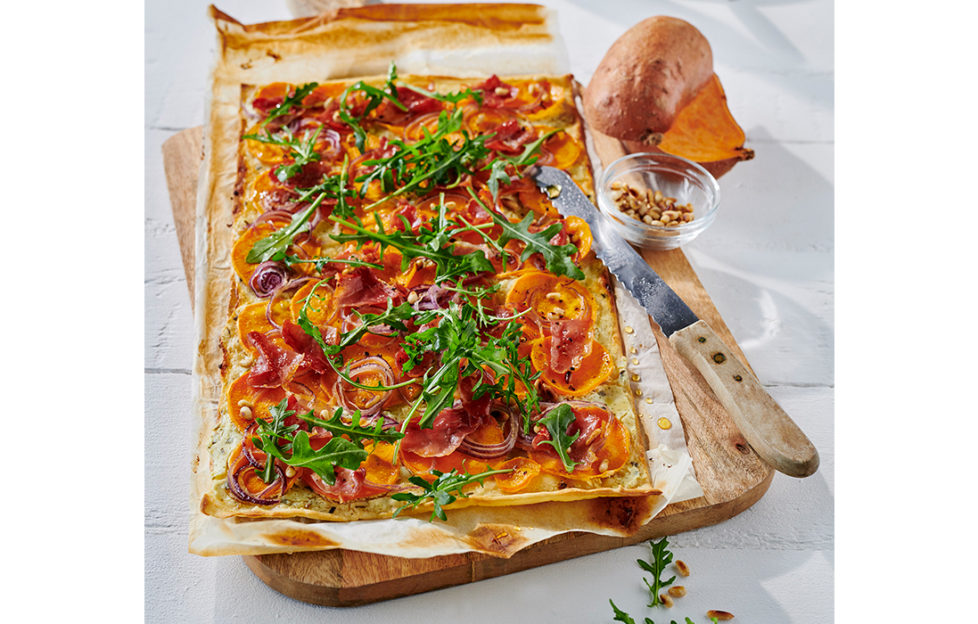 Rectangular pastry base with rich orange sliced sweet potatoes, onions and green rocket scattered over
