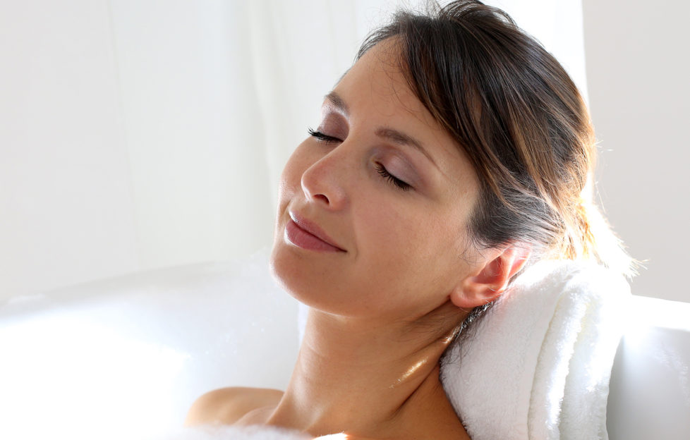Woman relaxing in bubble bath, leaning head back on folded towel, eyes closed