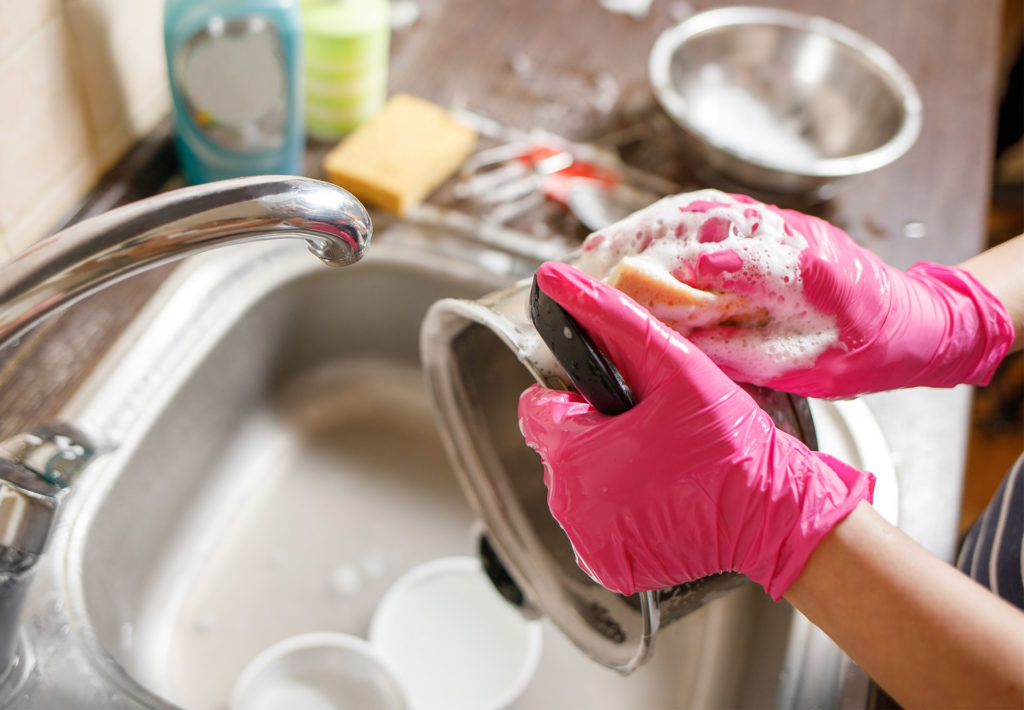 \woman at kitchen sink in pink rubber gloves scrubbing the bottom of a small saucepan