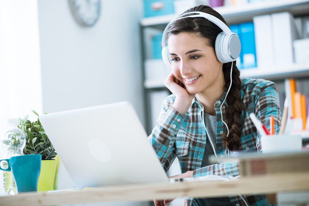 Teenage smiling girl using a laptop and wearing headphones, 