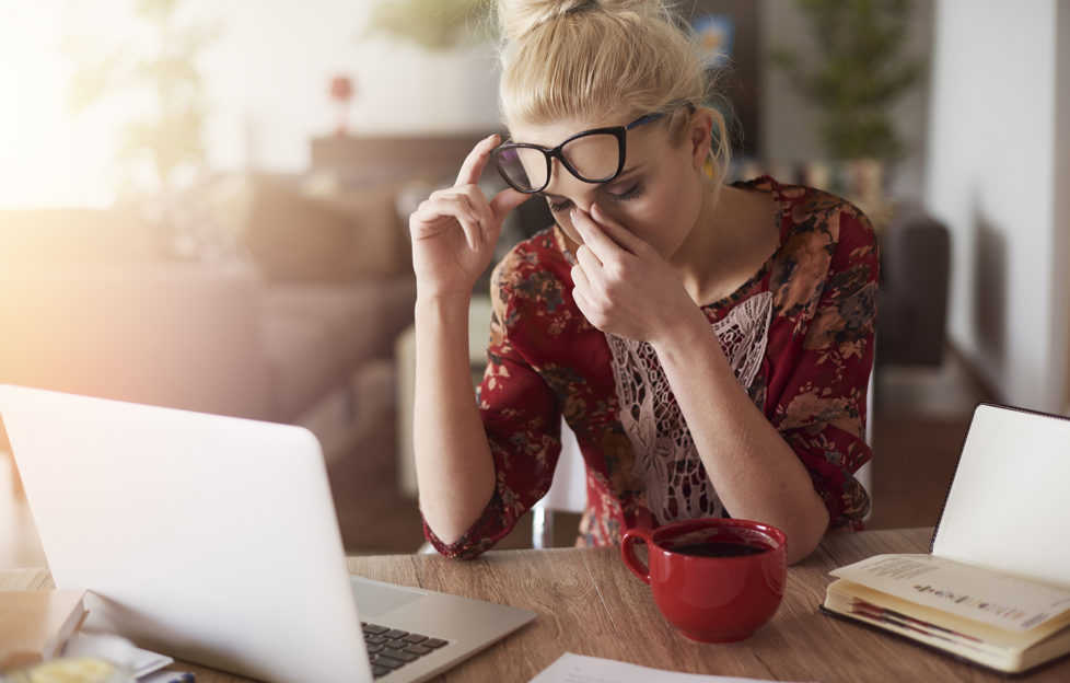 Blonde woman at laptop rubbing eyes, looking like she has a headache