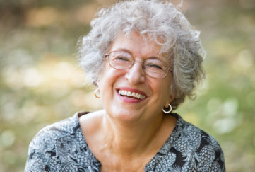 Portrait of senior woman smiling and looking at camera. Cheerful mature woman wearing eyeglasses in the park. Happy old woman with grey hair smiling. Carefree and positive retired woman.