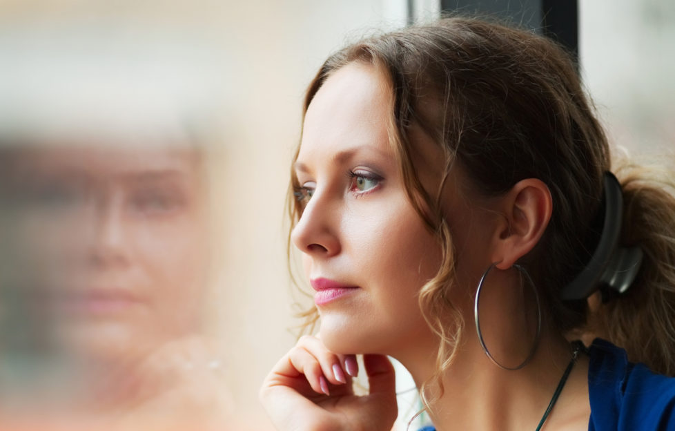 Sad beautiful woman looking through a window;