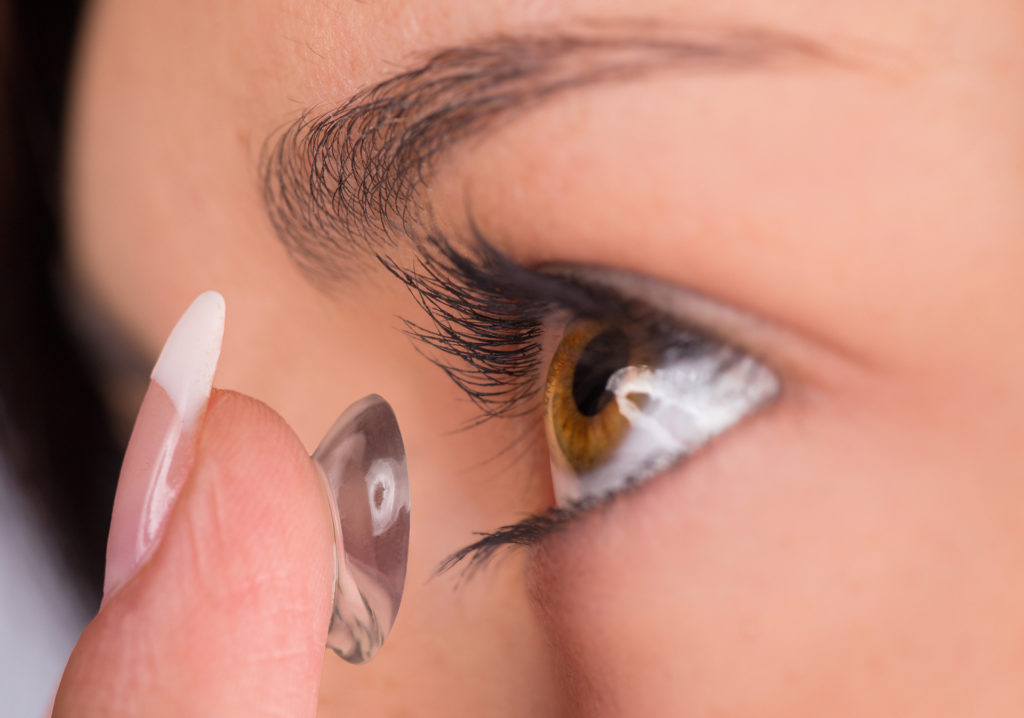 Young woman putting contact lens in her eye. 