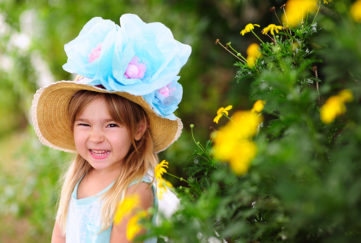Happy girl with straw hat and 3 huge blue and purple flowers on it, Easter bonnet
