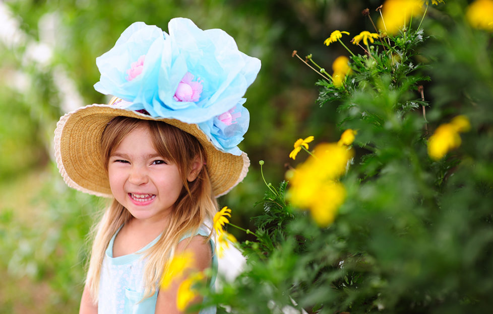 Happy girl with straw hat and 3 huge blue and purple flowers on it, Easter bonnet