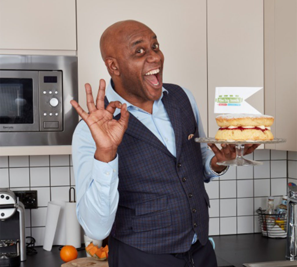 Celebrity chef Ainsley Harriott in his kitchenholds a sponge cake and gives a big grin and OK sign