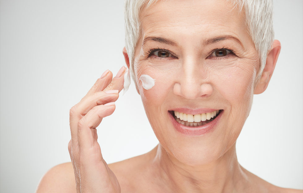 Head shot of beautiful senior woman putting on the cream.