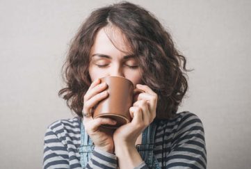 Woman drinking a cup of coffee or tea. Gray background
