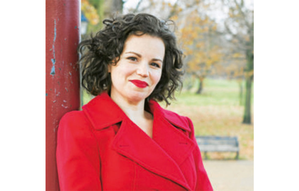 Dr Philippa Kaye, dark haired woman in red coat with red lipstick in a park