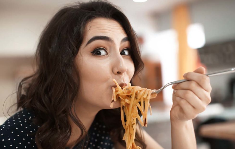 Funny young woman eating tasty pasta in cafe