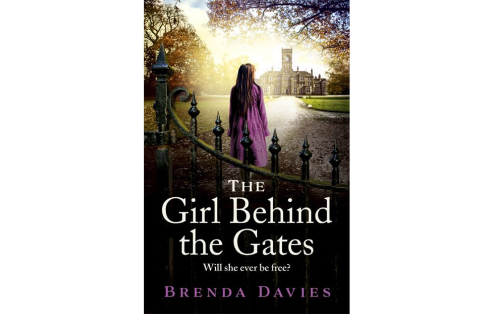 Cover of The Girl Behind The Gates, photo image of teenage girl in purple coat looking towards Victorian hospital building, mature trees around