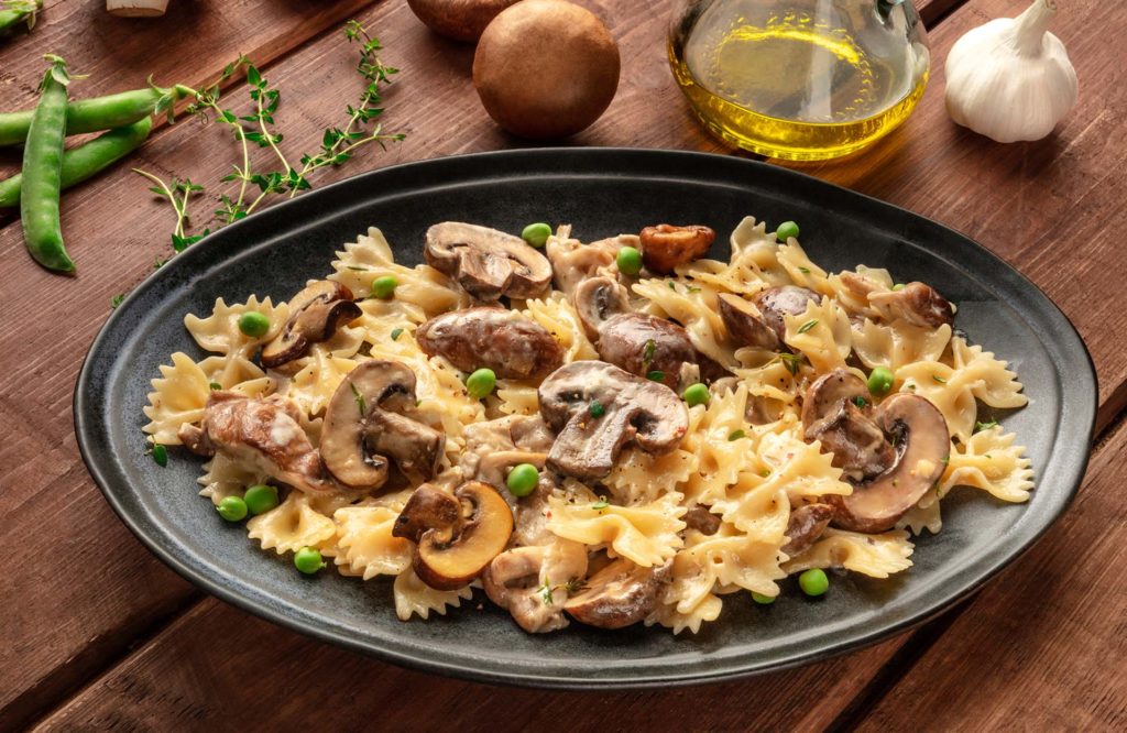 A plate of mushroom and cheese pasta. Farfalle with cremini and green peas with ingredients on a dark rustic wooden background