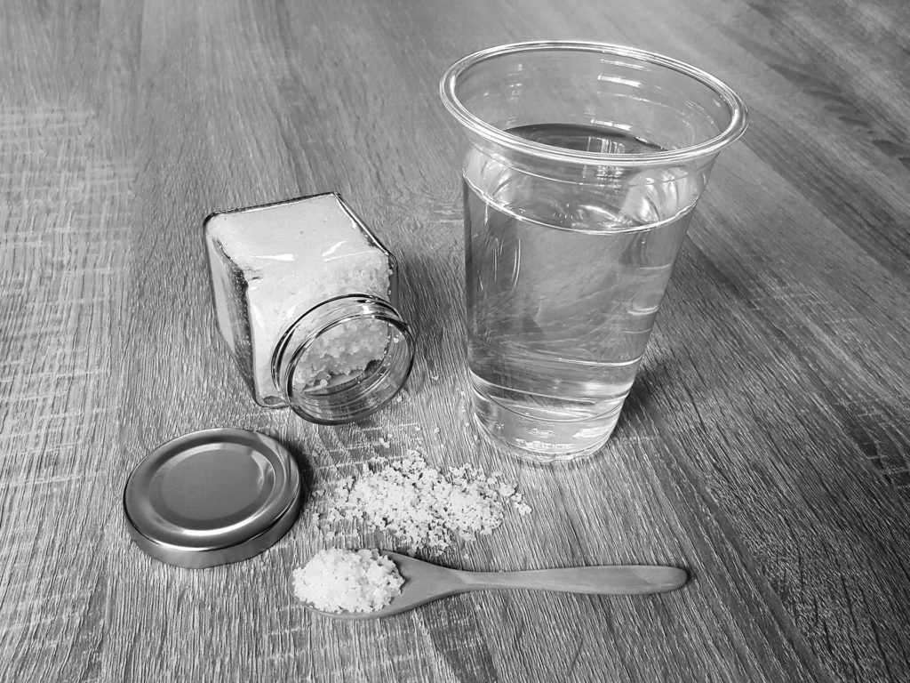 Black and white salt in the spoon and glass bottle with water on wooden table.; 