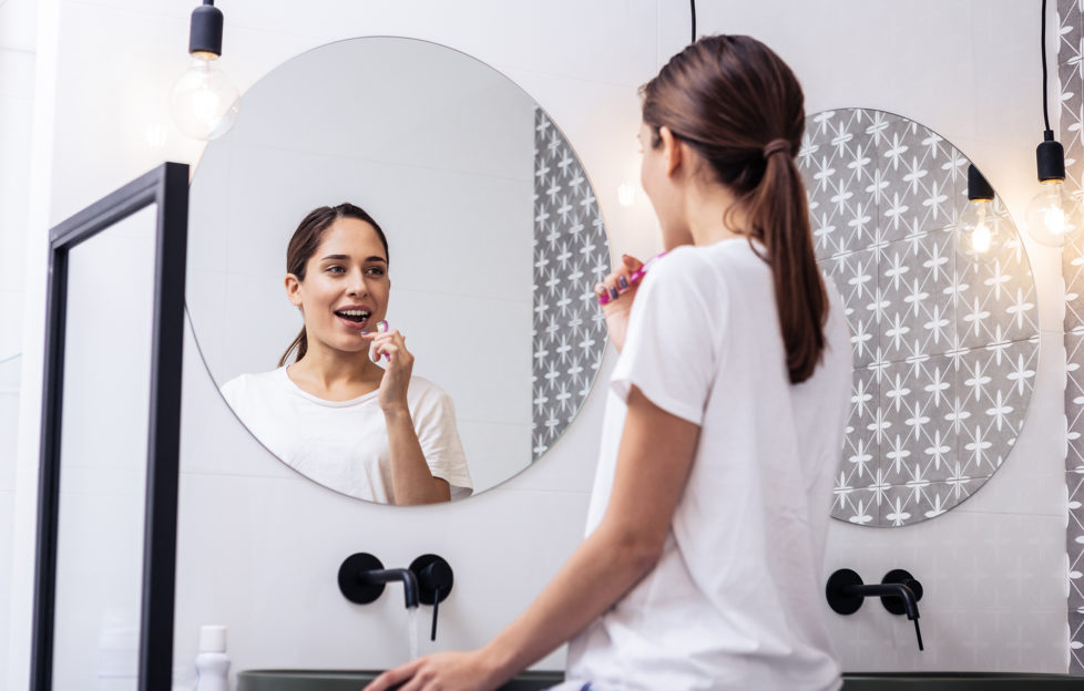 Circular mirror. Close up of appealing woman brushing teeth in front of circular mirror;