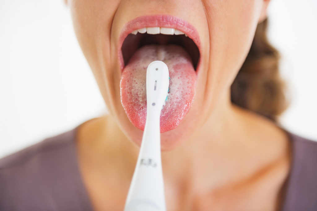Closeup on young woman cleaning tongue using toothbrush; 