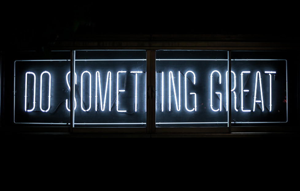Neon sign, white capitals on black, reading Do Something Great. Career concept.