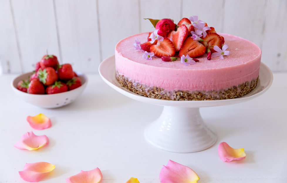 Yoghurt cake, cheesecake-like dessert on a cake stand, crunchy base, creamy pink layer and topped with fresh strawberries